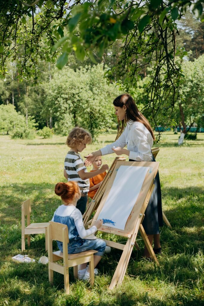 pexels-photo-8922793-8922793 Children painting with instructor in a sunny garden setting promoting creativity and learning.